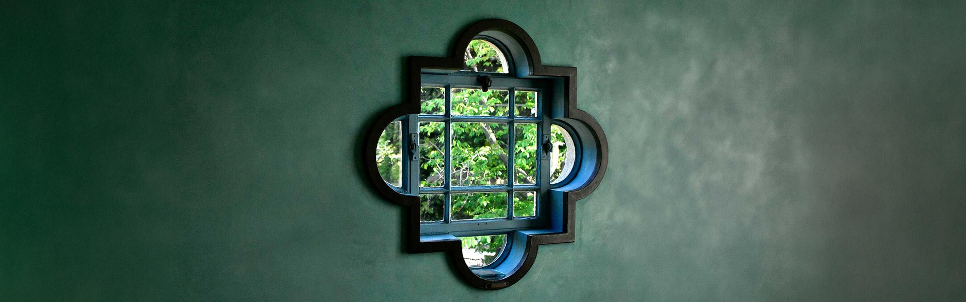 photo of a quatrefois shaped window showing greenary, by Geoff Oliver for Unsplash.